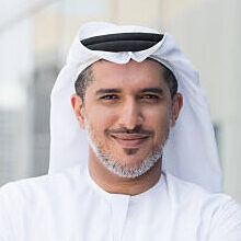 A photo of confident and smiling mid adult arab businessman. Emirati man is wearing tradition clothing. Portrait of middle eastern professional standing arms with crossed outside office building. Dubai, United Arab Emirates, Middle East